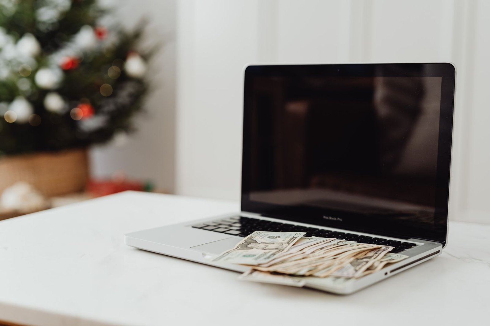 How to Earn Online Certification - A laptop on a desk covered with cash, featuring a Christmas tree in the background.