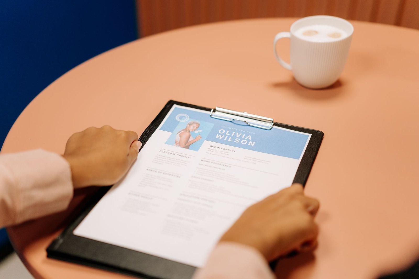 Interview Skills and CV Writing Certification - Close-up of hands holding resume during interview with coffee on table, highlighting workplace setting.