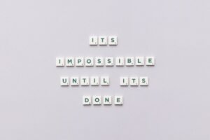 Overcoming Imposter Syndrome - Motivational phrase 'It's impossible until it's done' arranged with Scrabble tiles on a gray background.