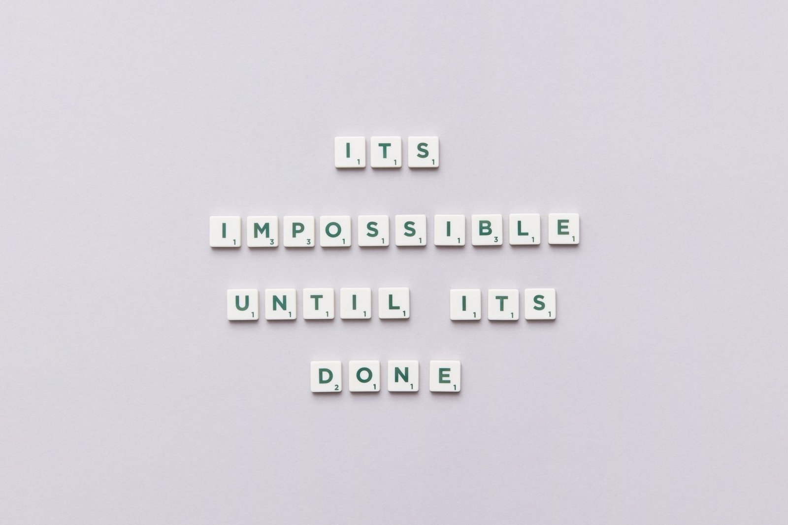 Overcoming Imposter Syndrome - Motivational phrase 'It's impossible until it's done' arranged with Scrabble tiles on a gray background.