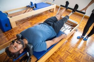 Pilates Foundation Level Certificate - Amputee man in a blue shirt doing physical therapy with a prosthetic leg on Pilates equipment indoors.