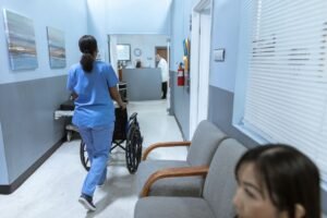 Duty of Care Certification - A nurse in scrubs pushes a wheelchair through a well-lit hospital corridor, attending to patient care.