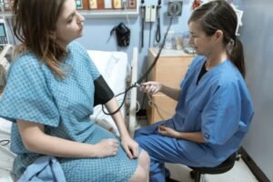 Nursing Assistant Certification - A nurse in blue scrubs checks the blood pressure of a female patient in a hospital room.