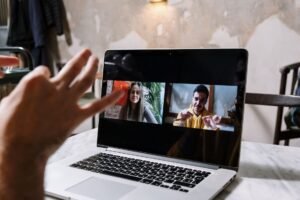 How to Manage Virtual Teams Certification - Hands gesturing during a video call on a laptop screen, showing two people in a virtual meeting.