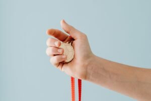 Conducting Rewarding Meetings Certification - A close-up image of a hand holding a gold medal with a red ribbon against a blue background.