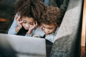 Safeguarding Children on the Internet Certification - From above of ethnic sister with brother browsing internet on netbook while lying on couch in house