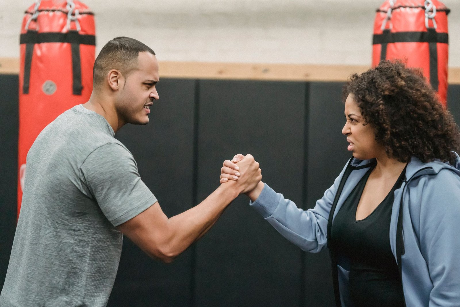 Working With Aggressive People Certification - Side view of angry African American couple clasping hands and looking at each other while showing strength during workout in boxing gym