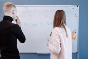 English Grammar — Improve Your English Certification - Two students studying English grammar at a whiteboard in a classroom setting.