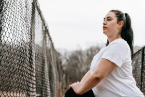 How to Improve Your Physical Health Certification - Side view concentrated plus sized sportswoman in white t shirt stretching legs near net fence in autumn countryside