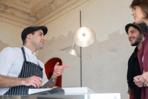 Connecting with Customers Certification - Chef in a stylish hat conversing with happy customers in a restaurant setting.