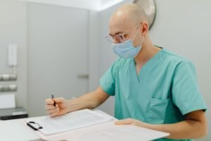 Recordkeeping and Documentation in Care Settings Certification - A healthcare professional in scrubs and face mask writes notes indoors, showcasing a clinical setting.