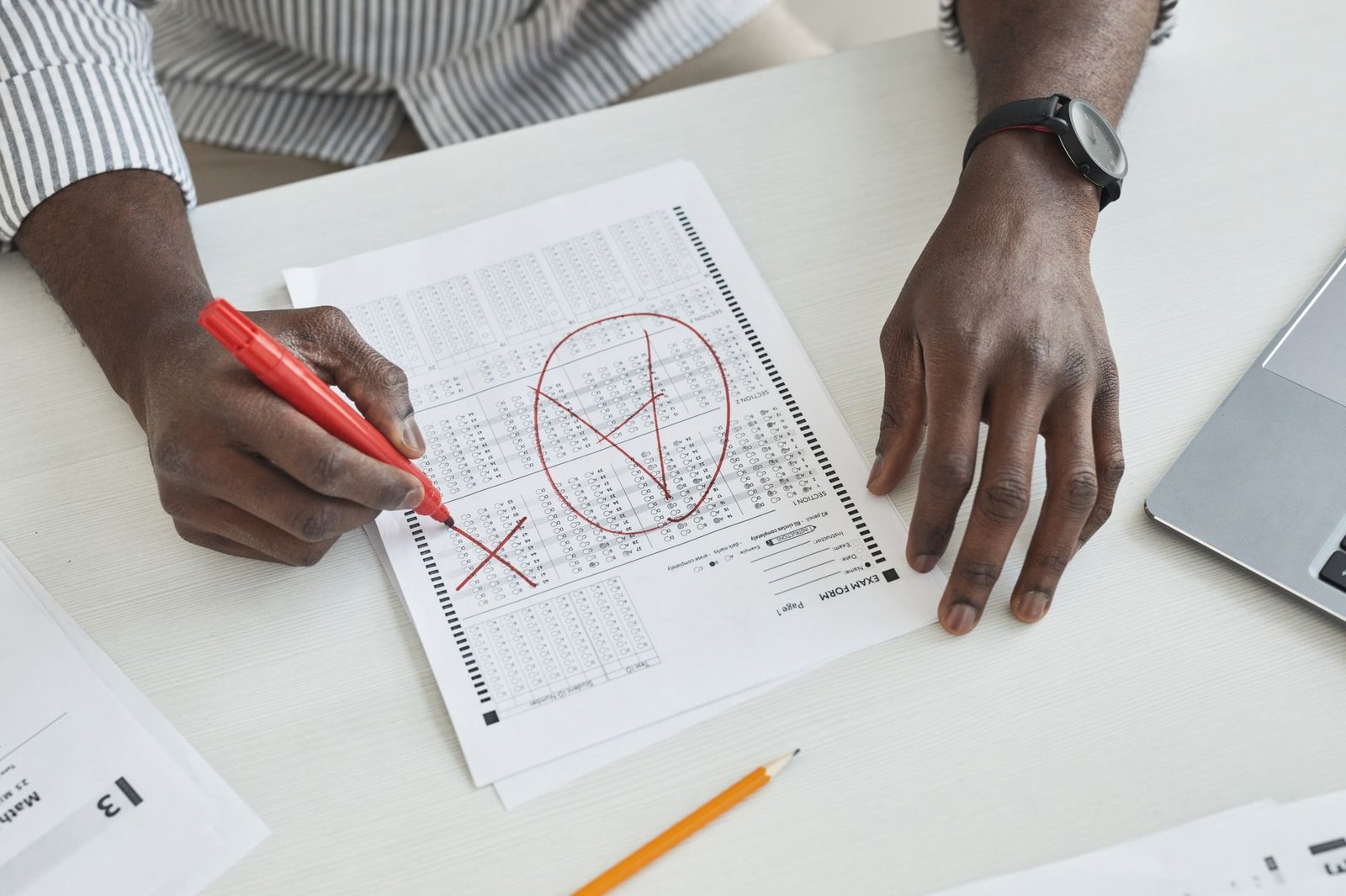 Exam Invigilator Training - Close-up of a teacher marking a test paper with a red marker on a desk.