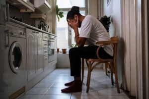 Eating Disorder Awareness Certification - A man sits in a kitchen, visibly stressed with head in hands, capturing an emotional moment indoors.