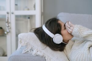 Reducing Stress (Techniques to Relax) Certification - Woman lying on couch with headphones, appearing relaxed or contemplative indoors, cozy atmosphere.