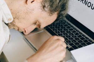 Dangers of Sleep Deprivation Certification - Exhausted employee resting head on laptop keyboard due to burnout and stress.