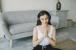 Introduction to Mindful Listening Certification - Young woman enjoying meditation with headphones at home, eyes closed, in a peaceful living room setting.