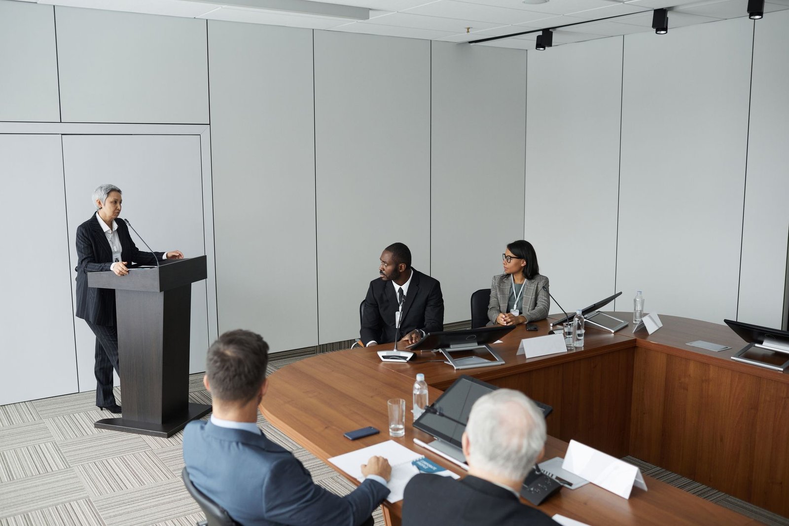 Establishing Credibility as a Speaker Certification - Diverse group of professionals in a formal meeting setting with a speaker at the podium.