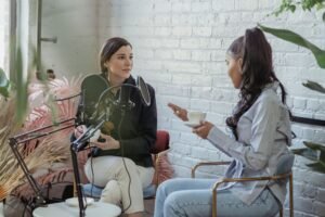 Listening Skills Certification - Serious host listening to African American female guest giving interview while sitting with cup of coffee near mic