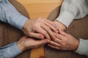 End of Life Care Certification - Close-up of elderly hands holding on a wooden table, symbolizing love and connection.