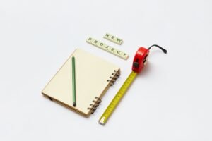 Project Management Foundation: Small Projects Certification - Flat lay of a notebook, pencil, tape measure, and scrabble tiles spelling 'new project'. Ideal for creative work concepts.