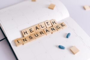 Understanding the National Insurance Contributions System Training - Close-up of health insurance spelled out with Scrabble tiles on a planner, alongside medication pills.