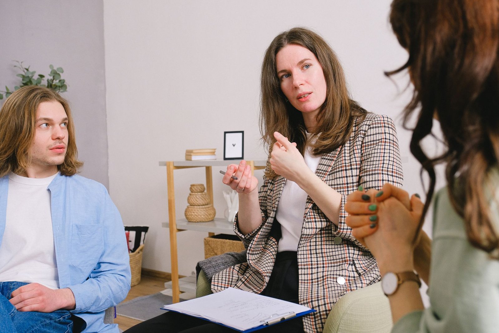 Cognitive Behavioural Therapy (CBT) Certification - Thoughtful woman psychologist in stylish clothes siting with clipboard and talking with couple in light room