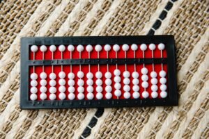 Basic Maths Certification - A close-up of a traditional abacus on a textured woven surface, showcasing white beads and red background.