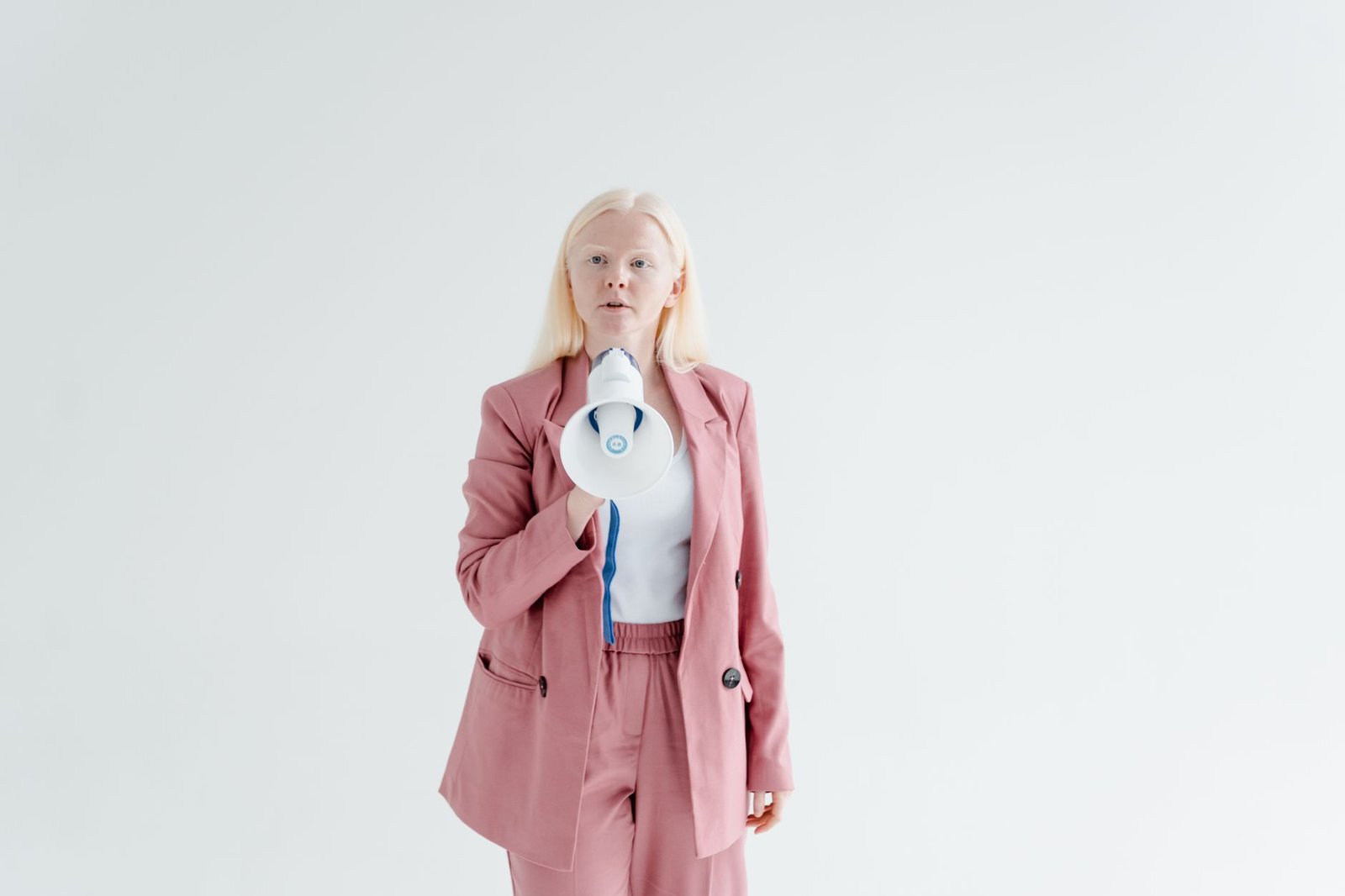 The Power of Influence & Motivating People to Buy Certification - Portrait of a confident woman in a pink suit holding a megaphone on a white background, promoting leadership and empowerment.