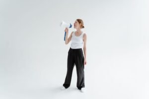The Art of Persuasion Certification - Woman in casual attire speaking through a megaphone in a bright studio setting.