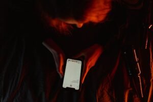Consequences of Careless Social Media Use in the Workplace Training - A person using a smartphone in dim, moody lighting with a dark background.