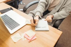Boost Your Work Efficiency Certification - Adult writing notes in a notebook at a desk with a laptop, emphasizing productivity.