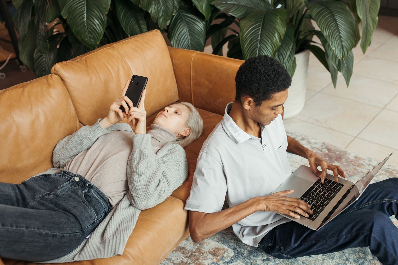 Hybrid Working - Two diverse co-workers relaxing and working on a sofa with a laptop and smartphone.