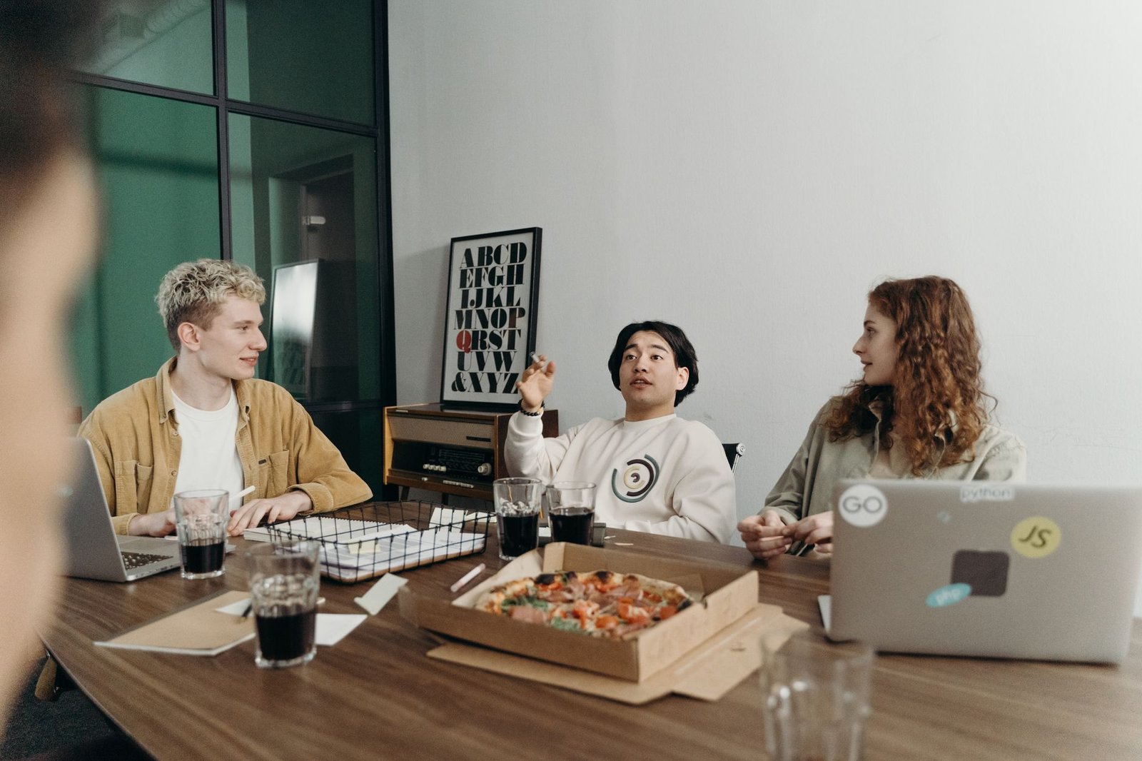 Creating Lively and Effective Meetings Certification - Young professionals brainstorm in a casual office setting with pizza and laptops.