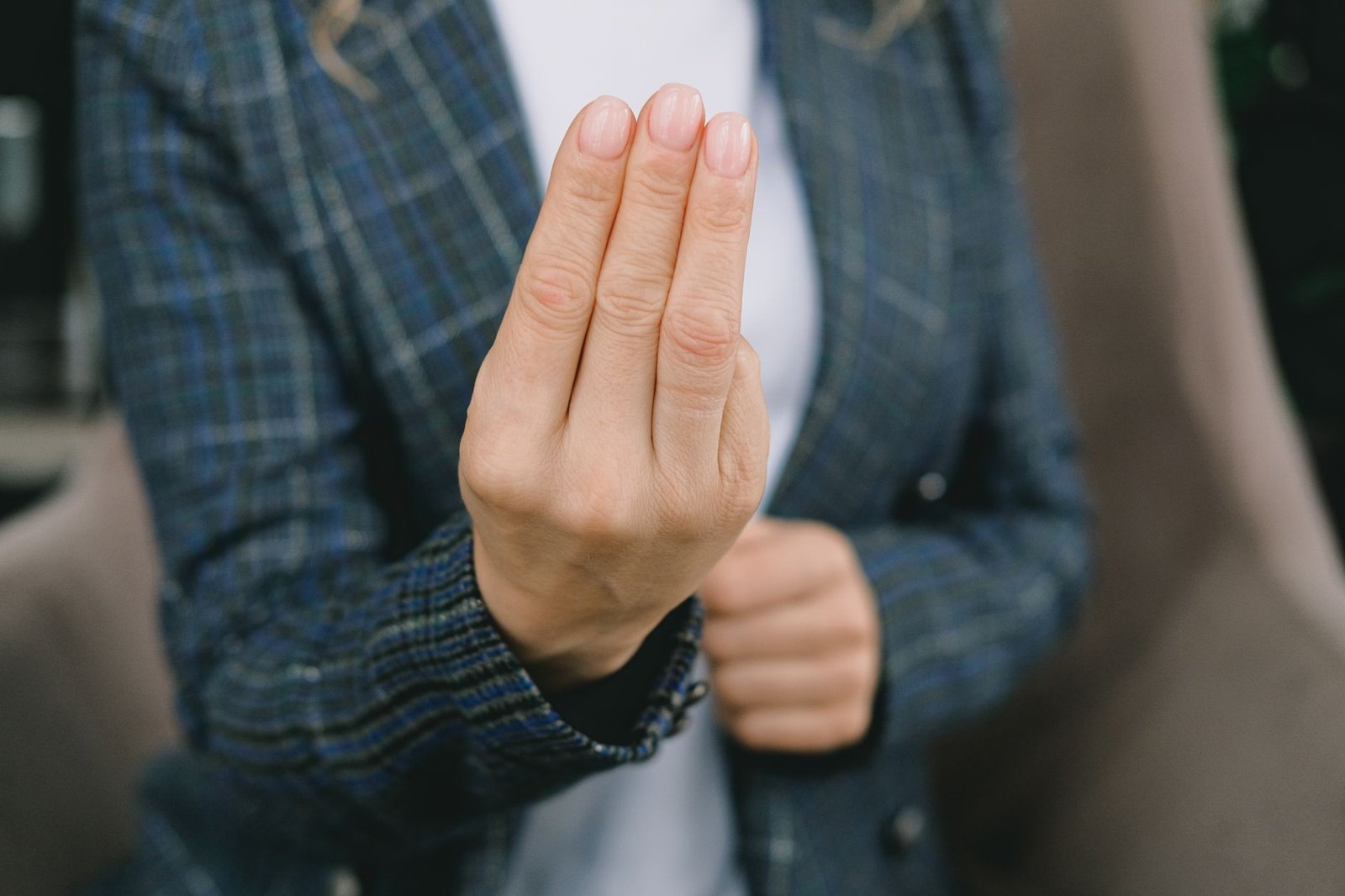 Body Language Certification - Crop anonymous woman in smart casual outfit sitting in armchair and showing three fingers gesture to camera