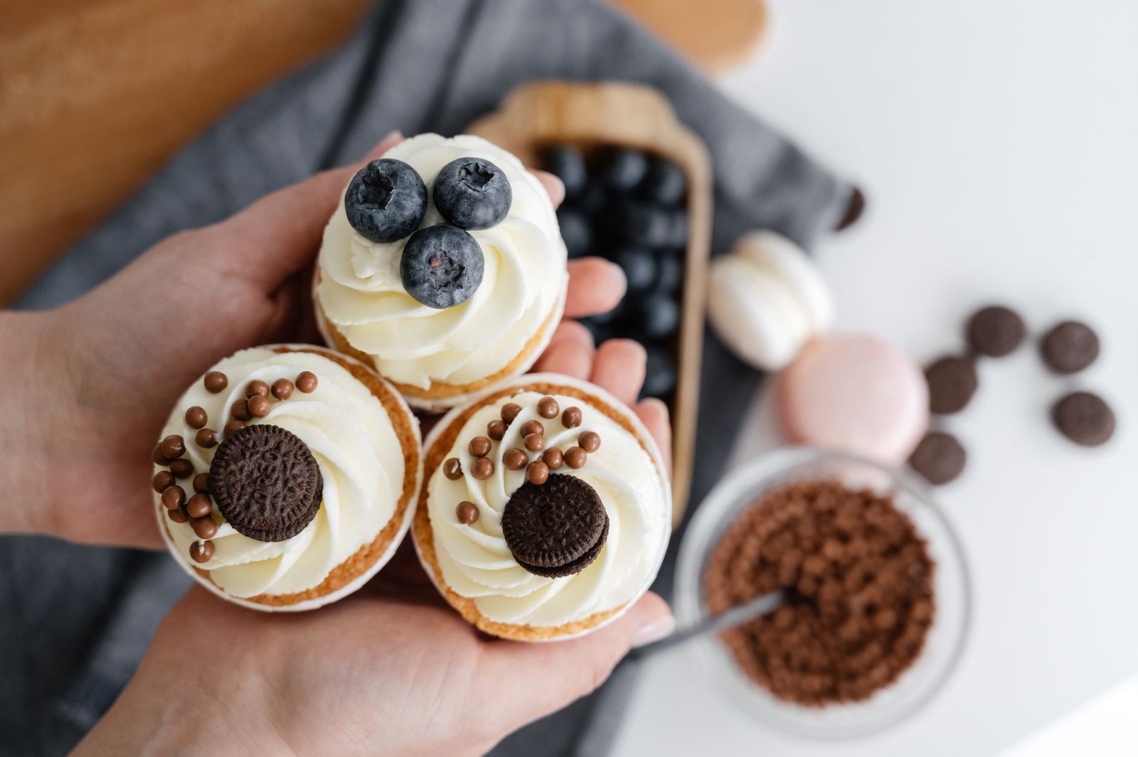 Cupcake Academy: Introduction to Running a Baking Business - Top view of crop anonymous person showing delicious cupcakes with blueberries and chocolate sweets against blurred background of various dessert