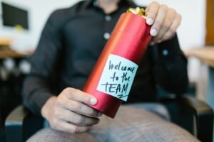 Onboarding Best Practices Certification - A red gift box held by a person with a welcome to the team note, ideal for new hire announcements.