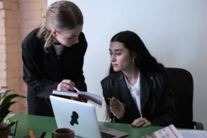The Effective Secretary Certification - Two female colleagues collaborating at an office desk with a laptop and notebook.