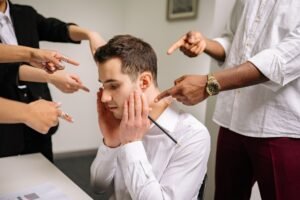 How to Handle Criticism at Work Certification - A stressed man at the office surrounded by pointing fingers, representing workplace bullying and stress.