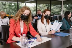Health and Safety for Events Certification - Participants in a business conference wearing face masks, taking notes indoors.