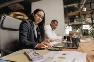 Introduction to Accounting Certification - Two business professionals collaborating with a laptop and calculator in a modern office.