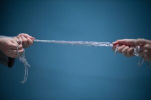 Thomas–Kilmann Conflict Mode Instrument Certification - Hands pulling a silver chain against a blue backdrop, symbolizing connection and strength.