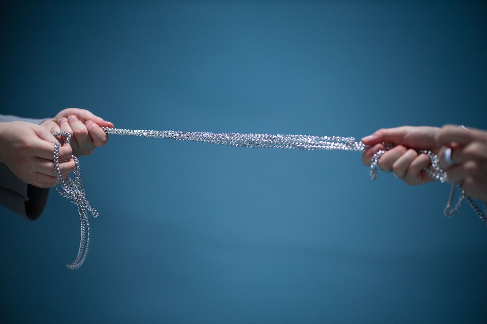 Thomas–Kilmann Conflict Mode Instrument Certification - Hands pulling a silver chain against a blue backdrop, symbolizing connection and strength.