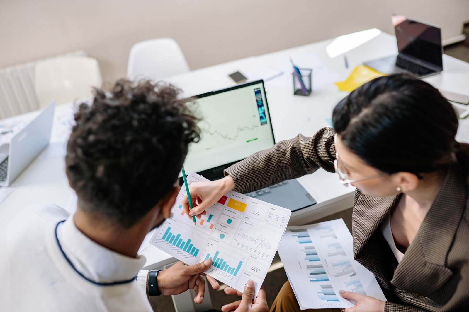 Marketing Certification Level 2 - Two colleagues in a meeting room discussing financial charts and graphs on a laptop and paper.