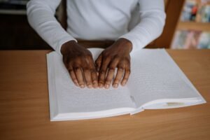 Learning Disabilities Awareness Certification - A person reading a Braille book indoors, focusing on accessibility and disability inclusion.