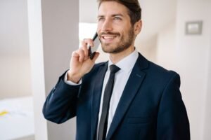 Networking for Sales Professionals Certification - Confident businessman in suit making a phone call indoors, smiling.