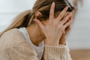 Mental Health In Construction Certification - Woman sitting indoors with face covered by hands, expressing stress and frustration.