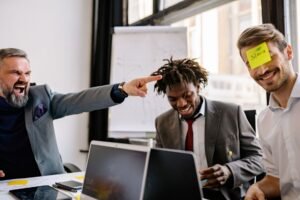 Emotional Intelligence Certification - Three diverse colleagues enjoy a lighthearted moment with sticky notes during an office meeting.