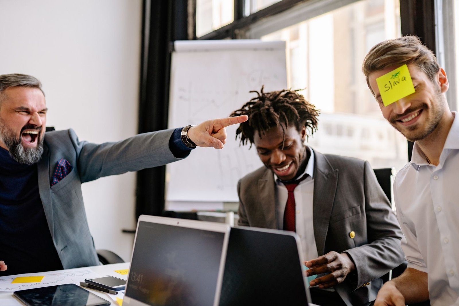 Emotional Intelligence Certification - Three diverse colleagues enjoy a lighthearted moment with sticky notes during an office meeting.