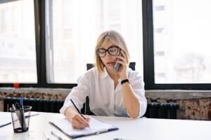 Medical Secretary Certification - A woman in an office setting multitasking with a phone call and taking notes.