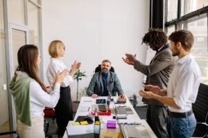 Motivating Colleagues to Perform Certification - Diverse business team applauding senior leader in modern office setting.